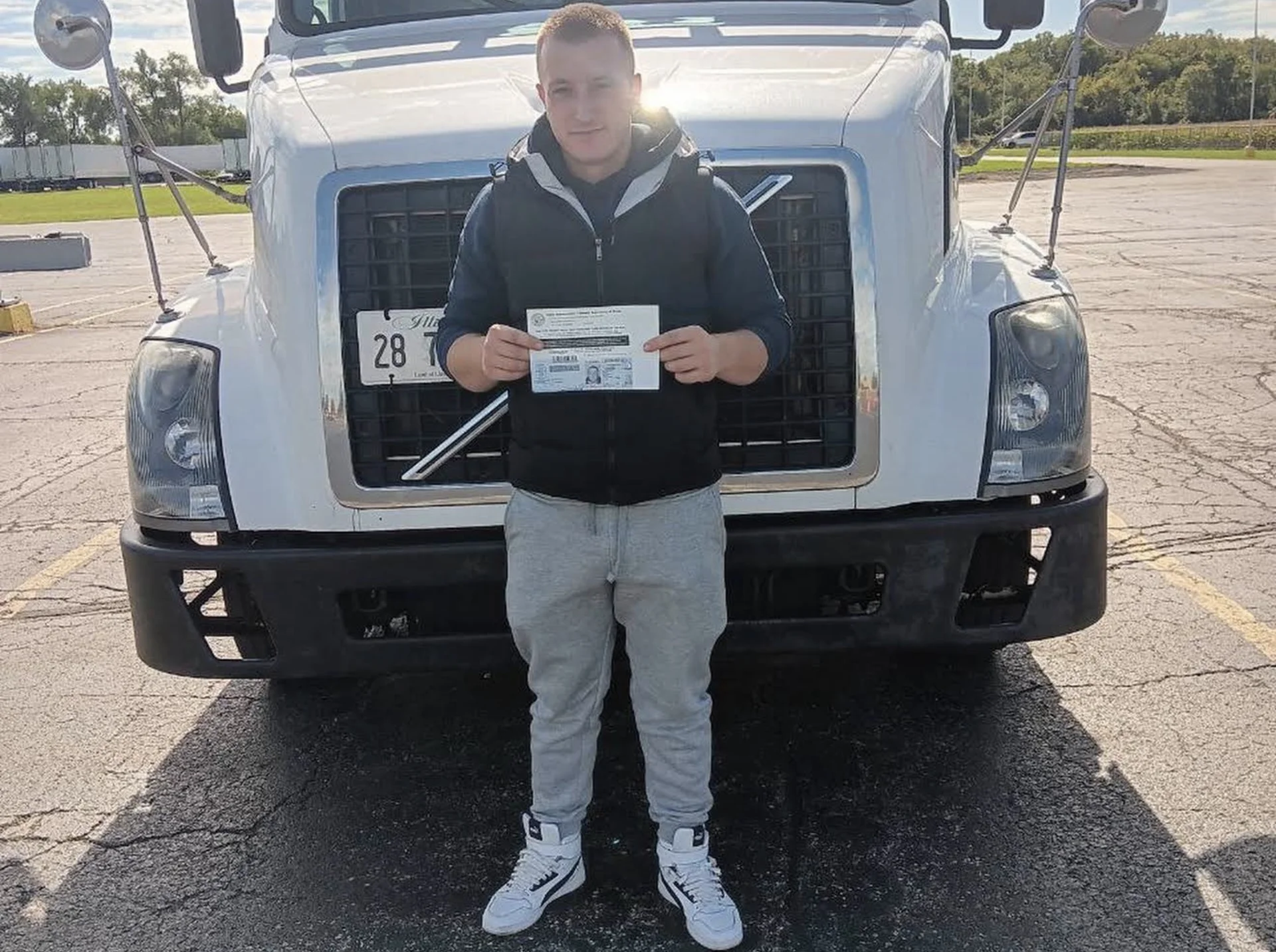 All-In CDL graduate holding their new CDL license in front of a training truck